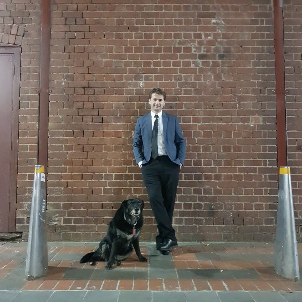 Steven Bailey in a suit with his dog against a brick wall
