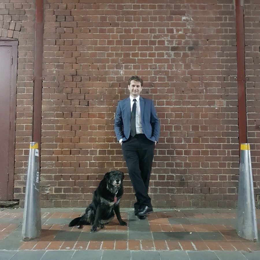 Steven Bailey in a suit with his dog against a brick wall
